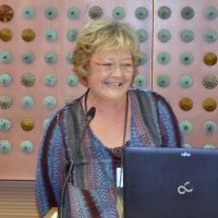 Eine Referentin steht am Mikrofon, spricht und lächelt dabei.