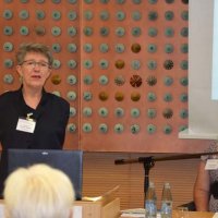 2 Referentinnen stehen vor der Leinwand und sprechen in Mikrofone.