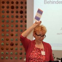 Eine Frau steht vor der Leinwand und hält einen Flyer in die Luft.