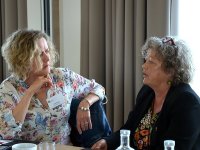 2 Frauen sitzen nebeneinander und sprechen miteinander.
