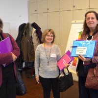 3 Frauen stehen im Bild und lächeln in die Kamera. Sie halten ihre Tagungsmappen in der Hand.